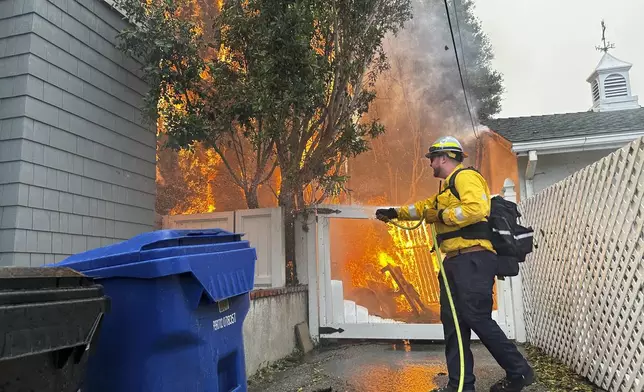 A structure burns as a firefighter battles the Palisades Fire in the Pacific Palisades neighborhood of Los Angeles Tuesday, Jan. 7, 2025. (AP Photo/Eugene Garcia)