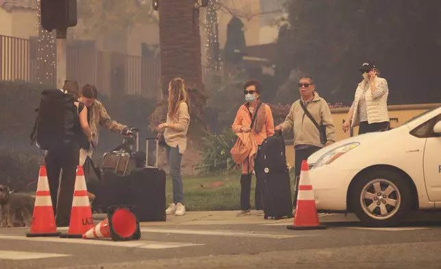 People wait with some belongings while fleeing the Palisades Fire in the Pacific Palisades neighborhood of Los Angeles, Tuesday, Jan. 7, 2025. (AP Photo/Etienne Laurent)