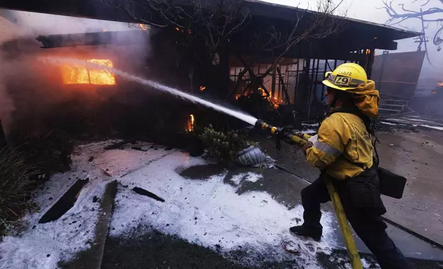 A firefighter tries to extinguish a fire as it damages a property in the Pacific Palisades neighborhood of Los Angeles Tuesday, Jan. 7, 2025. (AP Photo/Ethan Swope)