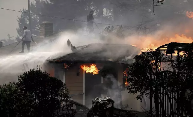 Eric Fiedler, left, and his son Christopher spray water on their roof in an attempt to save it along Sinaloa Avenue as his next door neighbors home burns during the Eaton fire in Altadena Wednesday morning Jan. 8, 2025. (Will Lester/The Orange County Register via AP)