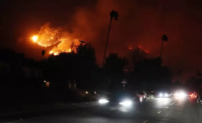 A car travels down East Mendocino Street as a wildfire burns in the hills near Eaton Canyon, Tuesday, Jan. 7, 2025, in Altadena, Calif. (AP Photo/Chris Pizzello)