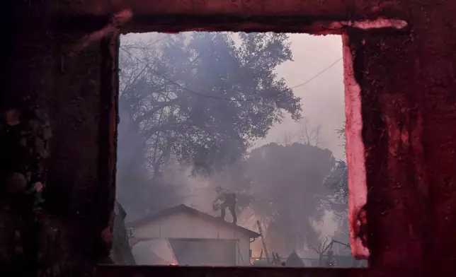 A firefighter is framed through the window of a fire-damaged property while battling the Eaton Fire Wednesday, Jan. 8, 2025 in Altadena, Calif. (AP Photo/Nic Coury)