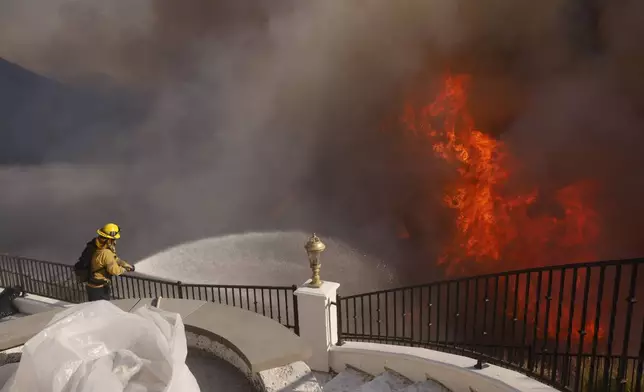 A firefighter makes a stand in front of the advancing Palisades Fire in the Pacific Palisades neighborhood of Los Angeles, Tuesday, Jan. 7, 2025. (AP Photo/Etienne Laurent)