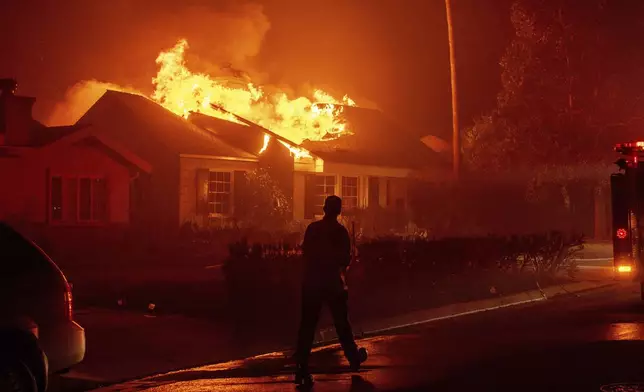 A firefighter walks toward a burning structure as the Eaton Fire advances Tuesday, Jan. 7, 2025 in Altadena, Calif. (AP Photo/Ethan Swope)