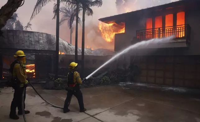 Firefighters hose down flames as the Palisades Fire destroys a residence in the Pacific Palisades neighborhood of Los Angeles, Tuesday, Jan. 7, 2025. (AP Photo/Etienne Laurent)