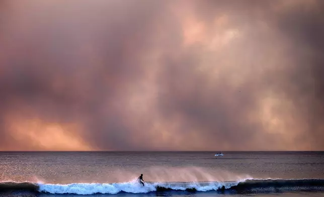 A surfer takes off on a wave in Santa Monica, Calif., during sunset under a blackened sky from the Palisades fire in the Pacific Palisades on Tuesday, Jan. 7, 2025. (AP Photo/Richard Vogel)