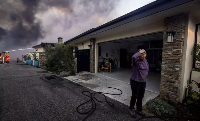 A resident stands in front of a garage as fire crews fight the Palisades Fire nearby in the Pacific Palisades neighborhood of Los Angeles, Tuesday, Jan. 7, 2025. (AP Photo/Ethan Swope)