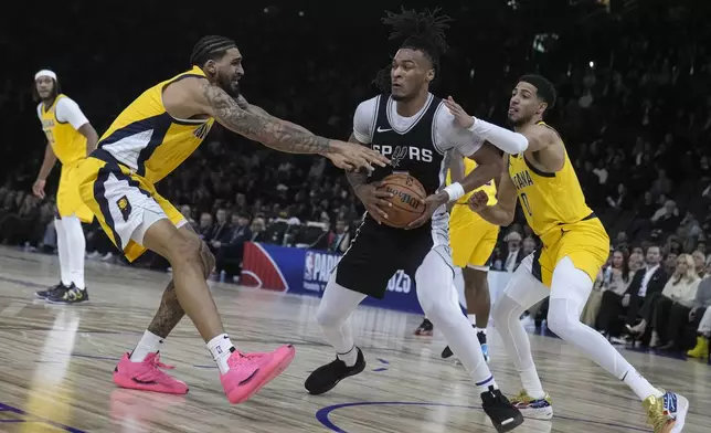 San Antonio Spurs guard Stephon Castle, center, is defended by Indiana Pacers forward Obi Toppin, left, and guard Tyrese Haliburton (0) during the second half of a Paris Games 2025 NBA basketball game in Paris, Saturday, Jan. 25, 2025. (AP Photo/Thibault Camus)