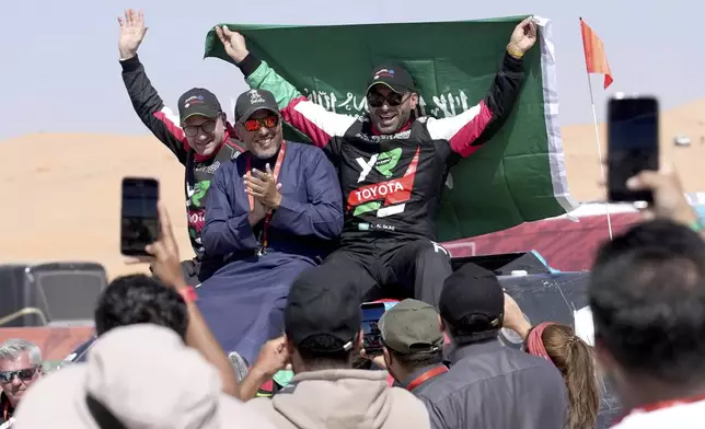 Driver Yazeed Al Rajhi, of Saudi Arabia, background right, co-driver Timo Gottschalk, of Germany, left, and Prince Khalid Bin Sultan Al Faisal, Head of Saudi motors Sports celebrate winning the Dakar Rally after the twelfth stage in Shubaytah, Saudi Arabia, Friday, Jan. 17, 2025. (AP Photo/Christophe Ena)