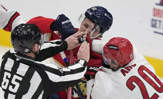 Carolina Hurricanes center Sebastian Aho (20) and Florida Panthers left wing Matthew Tkachuk (19) shuffle as linesman Tommy Hughes intervenes during the second period of an NHL hockey game, Thursday, Jan. 2, 2025, in Sunrise, Fla. (AP Photo/Wilfredo Lee)