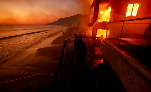 Firefighters work from a deck as the Palisades Fire burns a beachfront property Wednesday, Jan. 8, 2025 in Malibu, Calif. (AP Photo/Etienne Laurent)