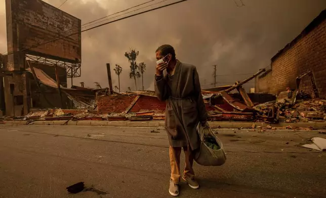 A man walks past a fire-ravaged business after the Eaton Fire swept through Wednesday, Jan. 8, 2025 in Altadena, Calif. (AP Photo/Ethan Swope)