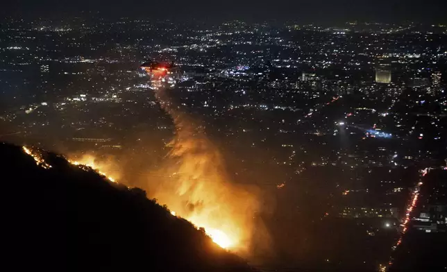 Water is dropped by helicopter on the burning Sunset Fire in the Hollywood Hills section of Los Angeles, Wednesday, Jan. 8, 2025. (AP Photo/Ethan Swope)