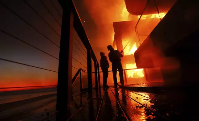 Firefighters work from a deck as the Palisades Fire burns a beach front property Wednesday, Jan. 8, 2025 in Malibu, Calif. (AP Photo/Etienne Laurent)