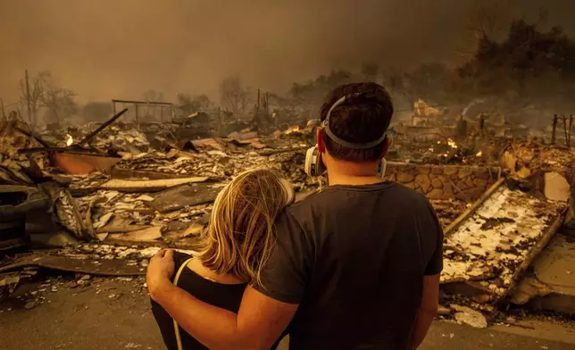 Megan Mantia, left, and her boyfriend Thomas, only first game given, return to Mantia's fire-damaged home after the Eaton Fire swept through the area, Wednesday, Jan. 8, 2025, in Altadena, Calif. (AP Photo/Ethan Swope)