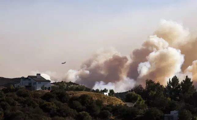 A firefighting plane makes drops over ridges as the Palisades Fire burns in the hills between Pacific Palisades and Malibu Wednesday, Jan. 8, 2025 in Topanga, Calif. (AP Photo/Etienne Laurent)