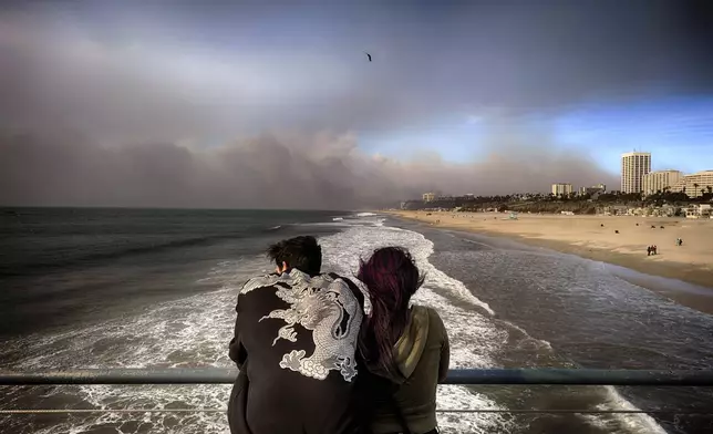 Visitors to the Santa Monica pier look out at smoke from a wildfire in the Pacific Palisades blows over the beach in Santa Monica, Calif., on Wednesday, Jan. 8, 2025. (AP Photo/Richard Vogel)