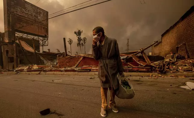 A man walks past a fire-ravaged business after the Eaton Fire swept through Wednesday, Jan. 8, 2025, in Altadena, Calif. (AP Photo/Ethan Swope)