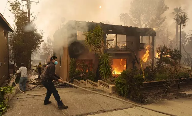 Pedestrians help a firefighter stretch a hose as an apartment building burns, Wednesday, Jan. 8, 2025, in the Altadena section of Pasadena, Calif. (AP Photo/Chris Pizzello)