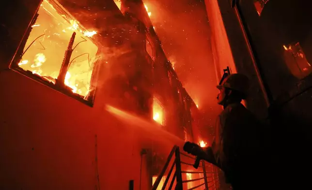 A firefighter works from a deck as the Palisades Fire burns a beachfront property Wednesday, Jan. 8, 2025, in Malibu, Calif. (AP Photo/Etienne Laurent)