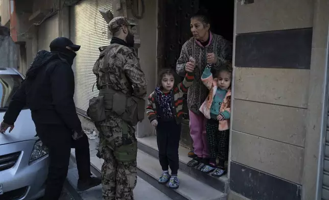 People stand outside their homes as members of the new security forces take part in an operation to detain, according to the state media, militiamen affiliated with ousted president Bashar Assad, at a residential area, in Homs, Syria, Thursday, Jan. 2, 2025. (AP Photo/Leo Correa)