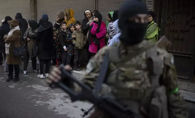 People stand outside their homes at a residential area as members of the new security forces take part in an operation to detain, according to the state media, militiamen affiliated with ousted president Bashar Assad in Homs, Syria, Thursday, Jan. 2, 2025. (AP Photo/Leo Correa)