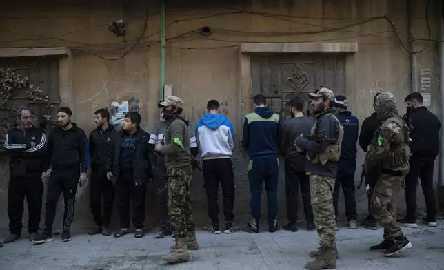 People stand in line as members of the new security forces check their IDs during an operation to detain, according to the state media, militiamen affiliated with ousted president Bashar Assad, at a residential area, in Homs, Syria, Thursday, Jan. 2, 2025. (AP Photo/Leo Correa)