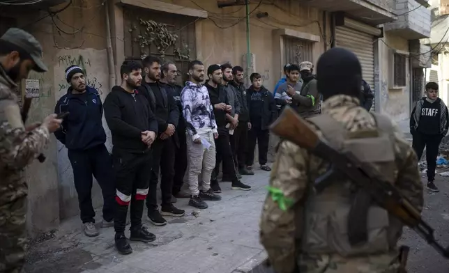 People stand in line before members of the new security forces check their IDs during an operation to detain, according to the state media, militiamen affiliated with ousted president Bashar Assad, at a residential area, in Homs, Syria, Thursday, Jan. 2, 2025. (AP Photo/Leo Correa)