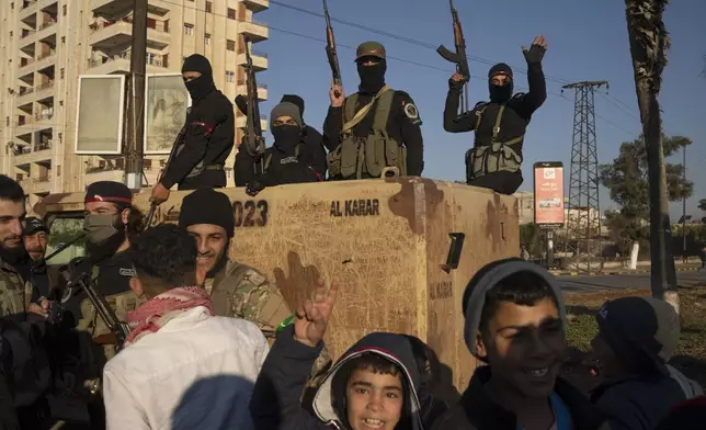 Members of the security forces of the newly formed Syrian government stand on a armoured vehicle next to the people as they take part in an operation to detain, according to the state media, militiamen affiliated with ousted president Bashar Assad in Homs, Syria, Thursday, Jan. 2, 2025. (AP Photo/Leo Correa)