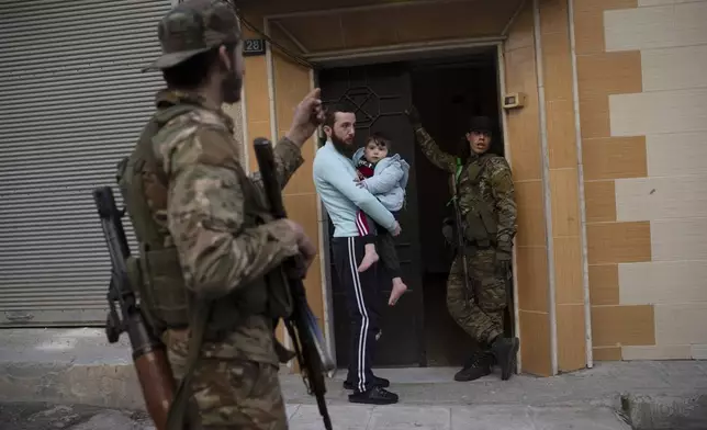 People stand outside their homes as members of the new security forces take part in an operation to detain, according to the state media, militiamen affiliated with ousted president Bashar Assad, at a residential area, in Homs, Syria, Thursday, Jan. 2, 2025. (AP Photo/Leo Correa)