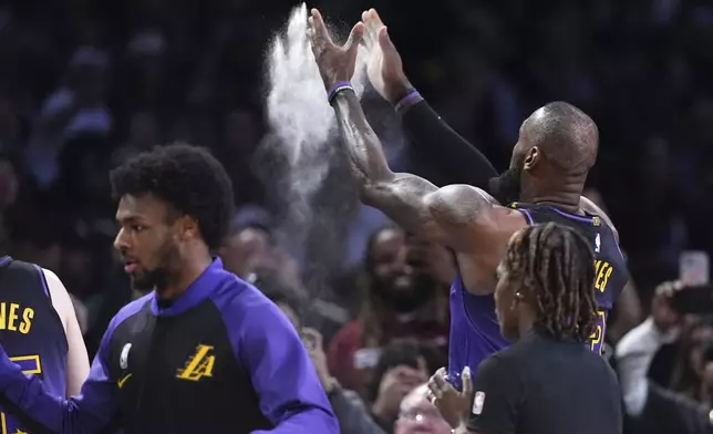 Los Angeles Lakers forward LeBron James, right, tosses powder in the air as guard Bronny James stands by prior to an NBA basketball game against the Portland Trail Blazers, Thursday, Jan. 2, 2025, in Los Angeles. (AP Photo/Mark J. Terrill)