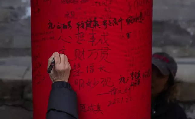 People write wishes on a red cloth roll as people visit a temple fair held at the Dongyue Temple on the first day of the Chinese Lunar New Year in Beijing on Wednesday, Jan. 29, 2025. (AP Photo/Andy Wong)