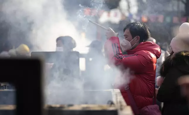 A man holding incense sticks prays on the first day of the Chinese Lunar New Year at Lama Temple in Beijing on Wednesday, Jan. 29, 2025. (AP Photo/Aaron Favila)