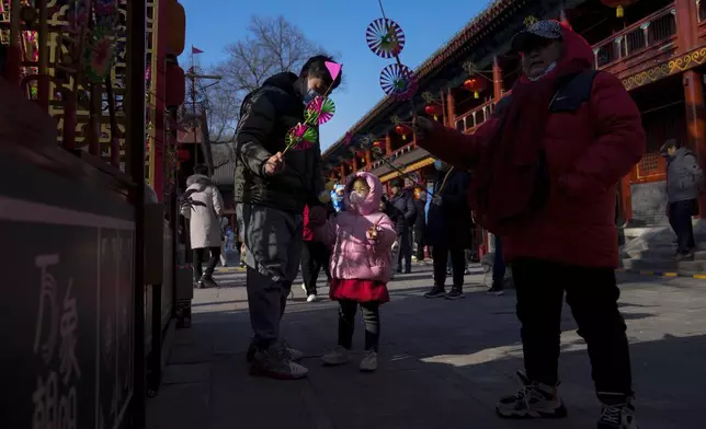 A man cheers a child with a wooden windmill toy as people visit a temple fair held at the Dongyue Temple on the first day of the Chinese Lunar New Year in Beijing on Wednesday, Jan. 29, 2025. (AP Photo/Andy Wong)