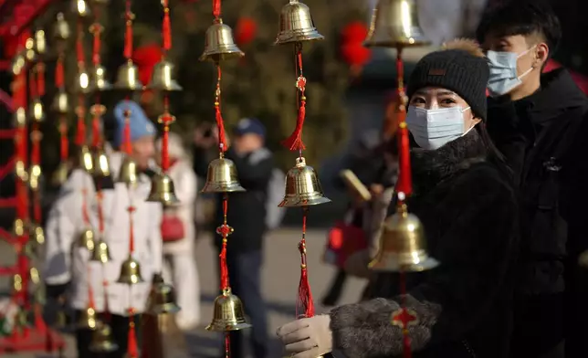A woman touches bells for luck as people gather at the Ditan Temple Fair on the first day of the Chinese Lunar New Year in Beijing on Wednesday, Jan. 29, 2025. (AP Photo/Aaron Favila)