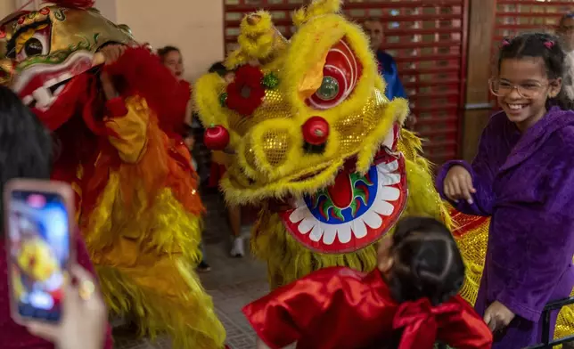 A performer dressed in a lion costume scares a girl as he dances the traditional Chinese Lion Dance at the start of Chinese Lunar New Year celebrations in Havana, Tuesday, Jan. 28, 2025. (AP Photo/Ramon Espinosa)