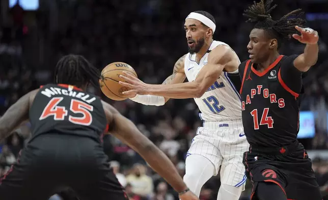 Orlando Magic guard Trevelin Queen (12) passes the ball as Toronto Raptors guard Ja'Kobe Walter (14) and guard Davion Mitchell (45) defend during the second half of an NBA basketball game, Friday, Jan. 3, 2025 in Toronto. (Frank Gunn/The Canadian Press via AP)