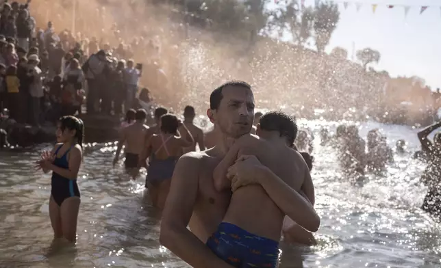 A father hugs his son as pilgrims jump to catch the cross during a water blessing ceremony marking the Epiphany celebrations, in Piraeus near Athens, on Monday Jan. 6, 2025. (AP Photo/Petros Giannakouris)