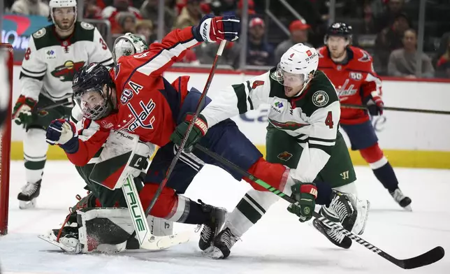 Minnesota Wild defenseman Jon Merrill (4) and Washington Capitals right wing Tom Wilson (43) battle in front of the net during the first period of an NHL hockey game, Thursday, Jan. 2, 2025, in Washington. (AP Photo/Nick Wass)