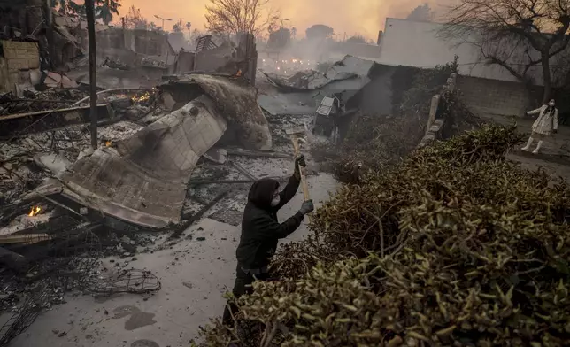 ADDS THE NAME OF A PERSON - Zuhayr Khan cuts down bushes as structures are seen on fire during the Eaton fire in Altadena, Calif., Wednesday, Jan. 8, 2025. (Stephen Lam/San Francisco Chronicle via AP)