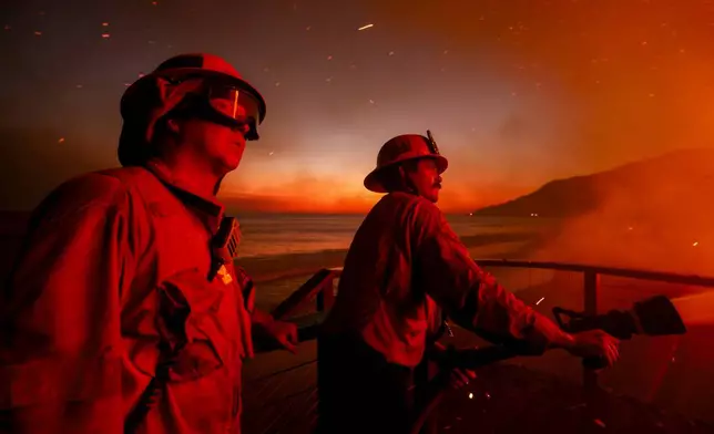 Firefighters work from a deck as the Palisades Fire burns a beachfront property Wednesday, Jan. 8, 2025 in Malibu, Calif. (AP Photo/Etienne Laurent)