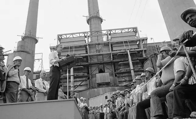 FILE - President Jimmy Carter talks to power plant workers against a backdrop of tall stacks at the Louisville Gas and Electric Company plant in Louisville, Ky., July 31, 1979. (AP Photo, File)