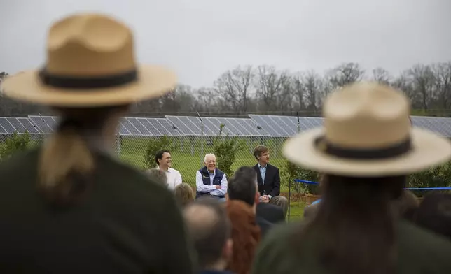 FILE - Former President Jimmy Carter, center, sits with his grandson Jason Carter, left, and George Mori, executive vice president at SolAmerica Energy during a ribbon cutting ceremony for a solar panel project on Jimmy Carter's farmland in his hometown of Plains, Ga., Feb. 8, 2017. (AP Photo/David Goldman, File)