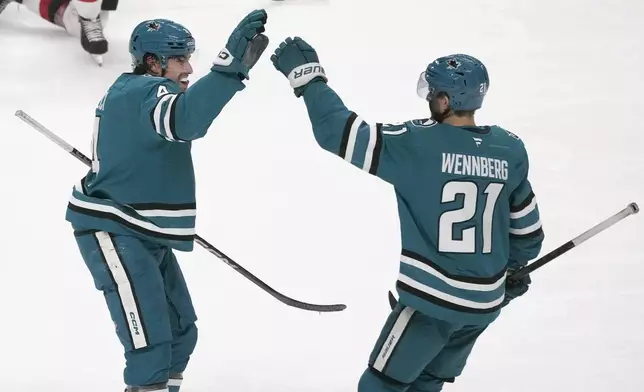 San Jose Sharks defenseman Cody Ceci, left, is congratulated by center Alexander Wennberg (21) after scoring against the New Jersey Devils during the third period of an NHL hockey game in San Jose, Calif., Saturday, Jan. 4, 2025. (AP Photo/Jeff Chiu)