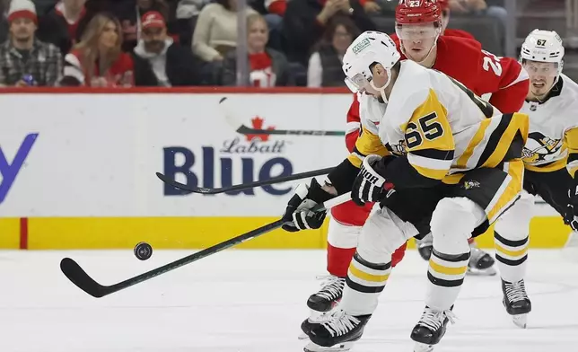 Pittsburgh Penguins defenseman Erik Karlsson (65) tries to get control of the puck passed by Detroit Red Wings left wing Lucas Raymond (23) during the first period of an NHL hockey game Tuesday, Dec. 31, 2024, in Detroit. (AP Photo/Duane Burleson)