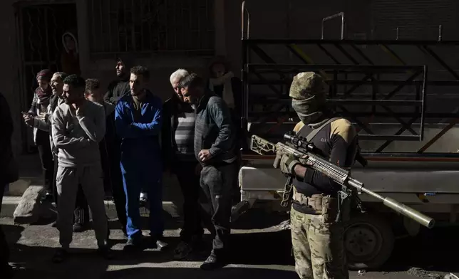 People stand outside their homes at a residential area as members of the new security forces take part in an operation to detain, according to the state media, militiamen affiliated with ousted president Bashar Assad in Homs, Syria, Thursday, Jan. 2, 2025. (AP Photo/Leo Correa)