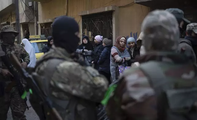 People stand outside their homes at a residential area as members of the new security forces take part in an operation to detain, according to the state media, militiamen affiliated with ousted president Bashar Assad in Homs, Syria, Thursday, Jan. 2, 2025. (AP Photo/Leo Correa)