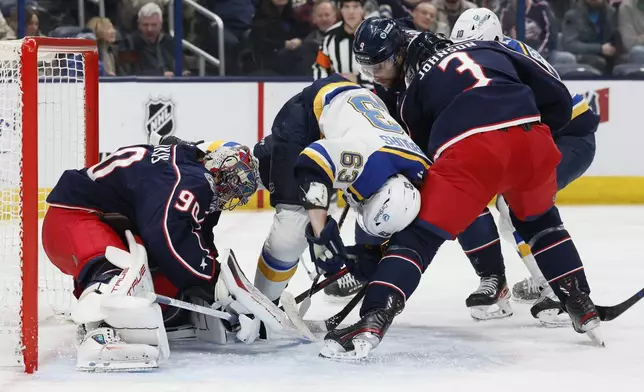 Columbus Blue Jackets' Elvis Merzlikins, left, makes a save as teammate Jack Johnson, right, and St. Louis Blues' Jake Neighbours collide in front of the net during the first period of an NHL hockey game Saturday, Jan. 4, 2025, in Columbus, Ohio. (AP Photo/Jay LaPrete)