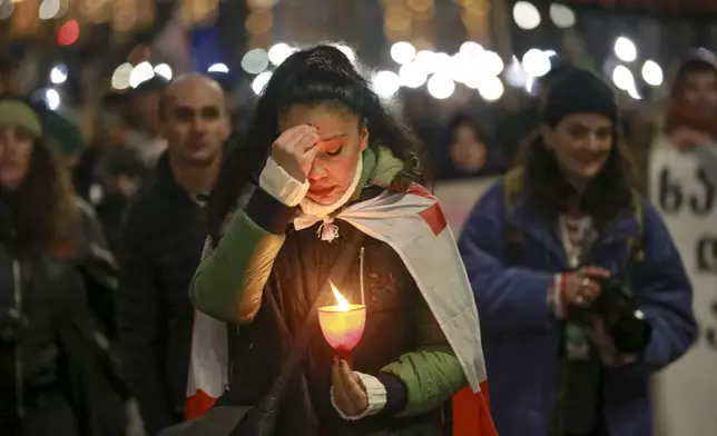 A woman crosses herself as she holds a candle walking in a street decorated for an Orthodox Christmas celebrating outside the Parliament building in Tbilisi, Georgia, Monday, Jan. 6, 2025. (AP Photo/Zurab Tsertsvadze)