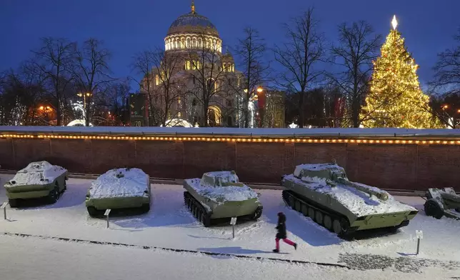 A boy runs past military vehicles displayed in Patriot Park near the Naval Cathedral of Saint Nicholas on the eve of Orthodox Christmas in Kronstadt, on the outskirts of St. Petersburg, Russia, Monday, Jan. 6, 2025. (AP Photo/Dmitri Lovetsky)